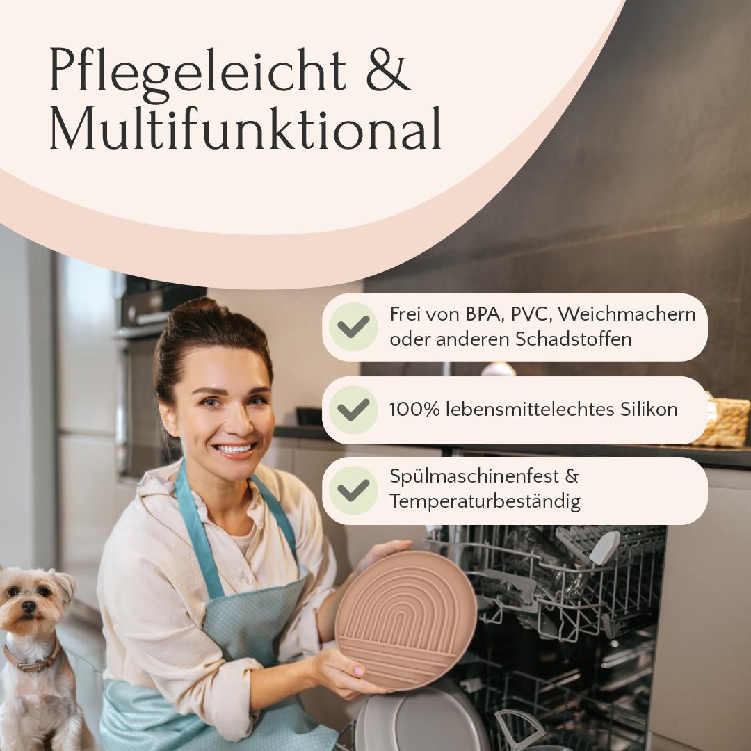 Eine lächelnde Frau lädt eine Pawfect Lickmat von FAVLY Petfood in den Geschirrspüler, während ihr kleiner Hund daneben steht.